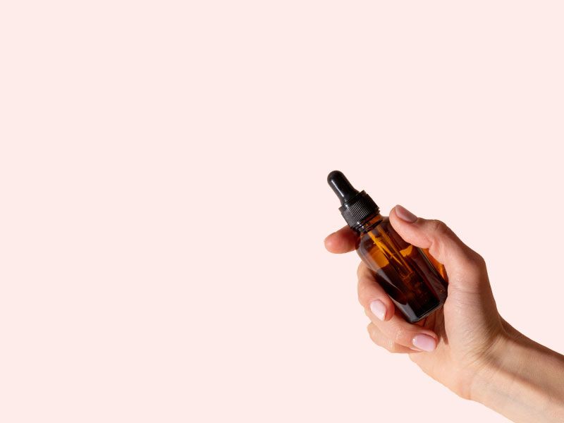 A hand holding an amber dropper bottle in front of a peach colored background