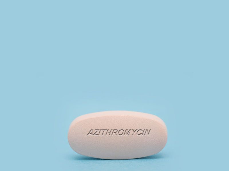 A white Azithromycin pill on a light blue surface
