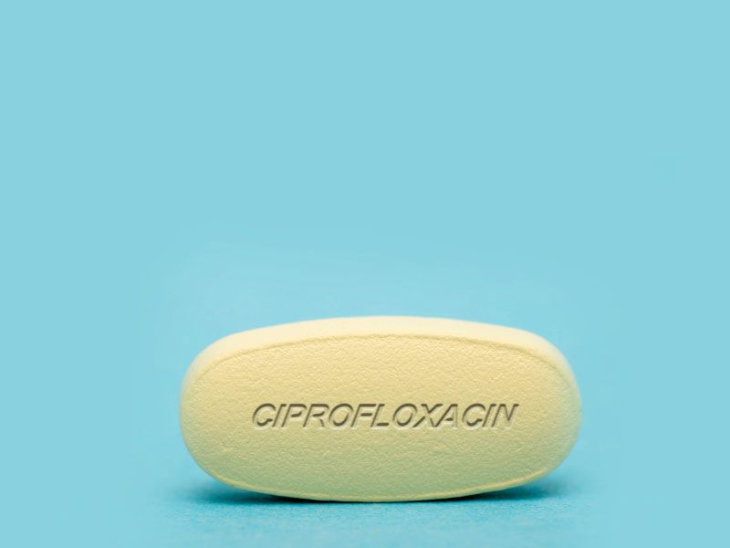 A yellow Ciprofloxacin pill on a light blue surface