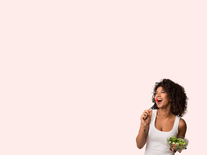 A woman wearing a white tank top is smiling while eating a salad