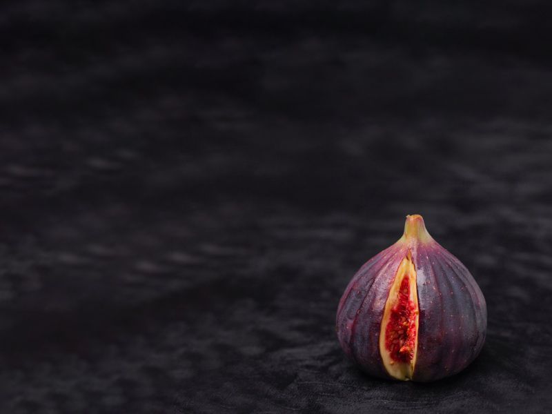 a fig sliced open to resemble a vulva on a dark background