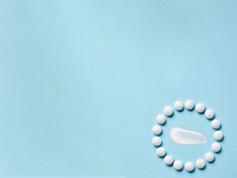 A cream swatch and round white pills on a light blue surface