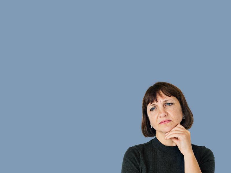 A woman wearing a black shirt with a worried demeanor in front of a blue background