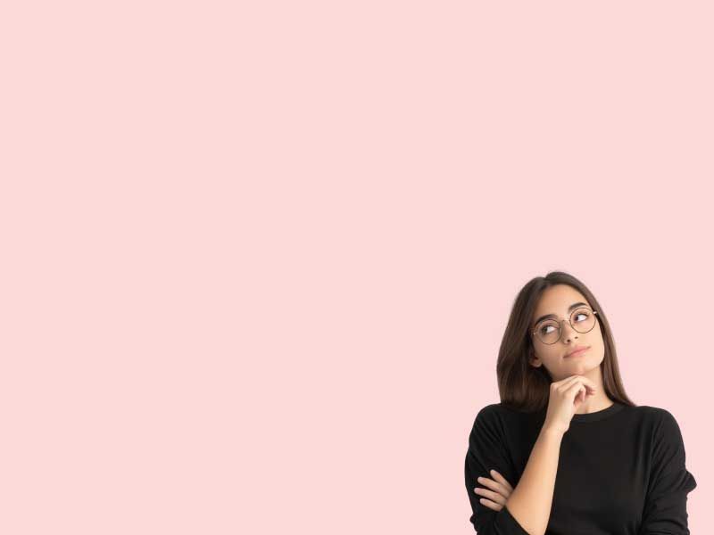A woman wearing a black sweater has her hand on her chin in contemplation in front of a pink background