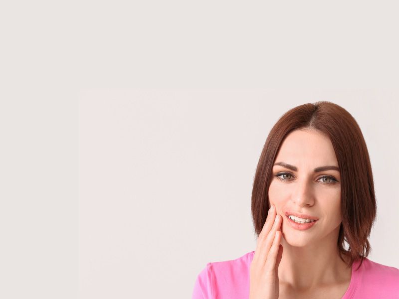 A woman wearing a pink shirt is touching her face with a pained expression