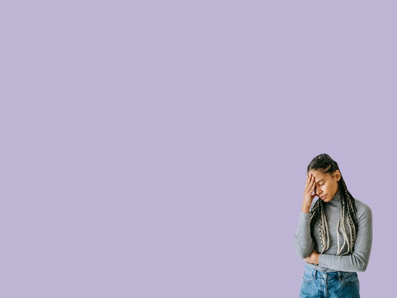 A woman wearing a gray shirt and jeans has her hand on her forehead indicating fatigue