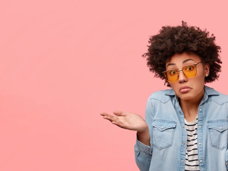 Woman wearing a striped shirt and a denim jacket is shrugging shoulders with a confused look on her face