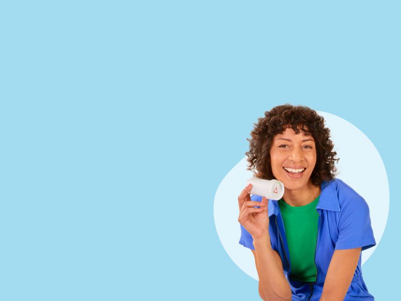 A woman wearing a green shirt and dark blue top is holding a bottle of spironolactone on a light blue background