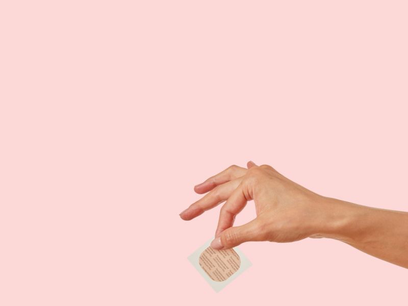 A woman wearing a white shirt and cream pants applying the birth control patch to her abdomen