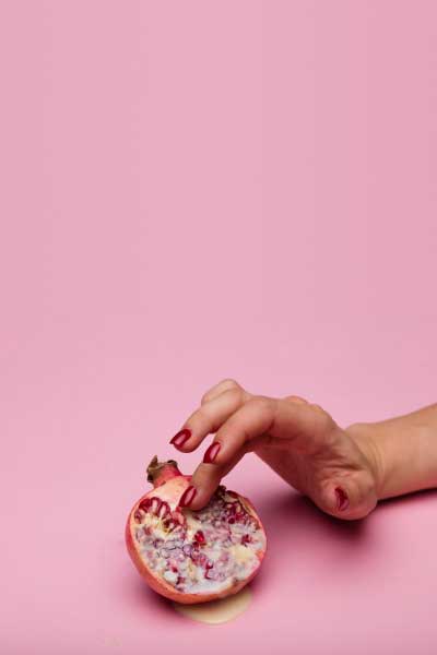A woman's hand is seductively touching an cut open fruit on a pink surface