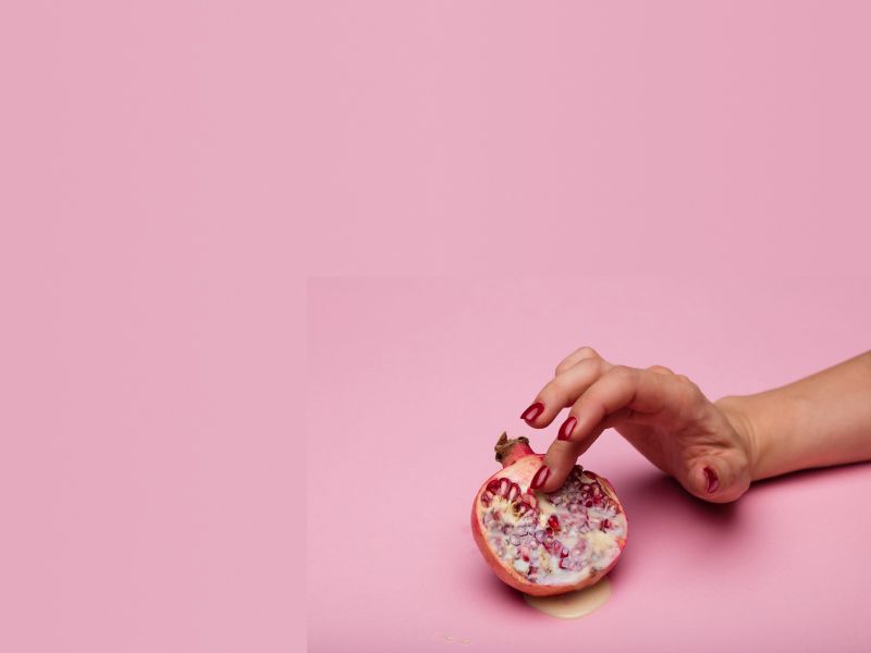 A woman's hand is seductively touching an cut open fruit on a pink surface