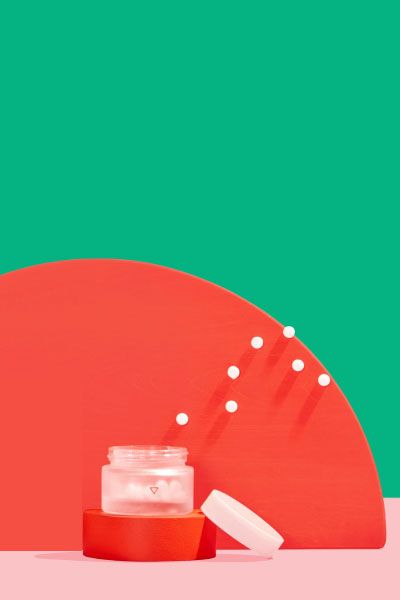 Wisp small glass pill jar with floating pills around colorful abstract shapes on a pink surface with a green background