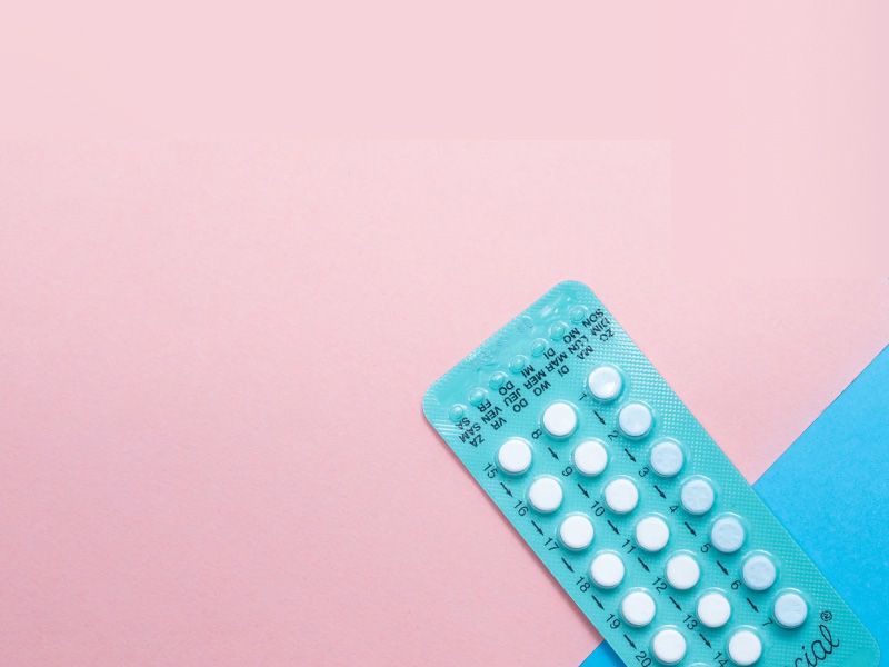 A blue birth control packet on a pink and light blue surface