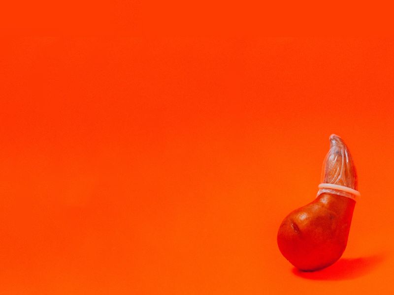 a red fruit wearing a condom on an orange background