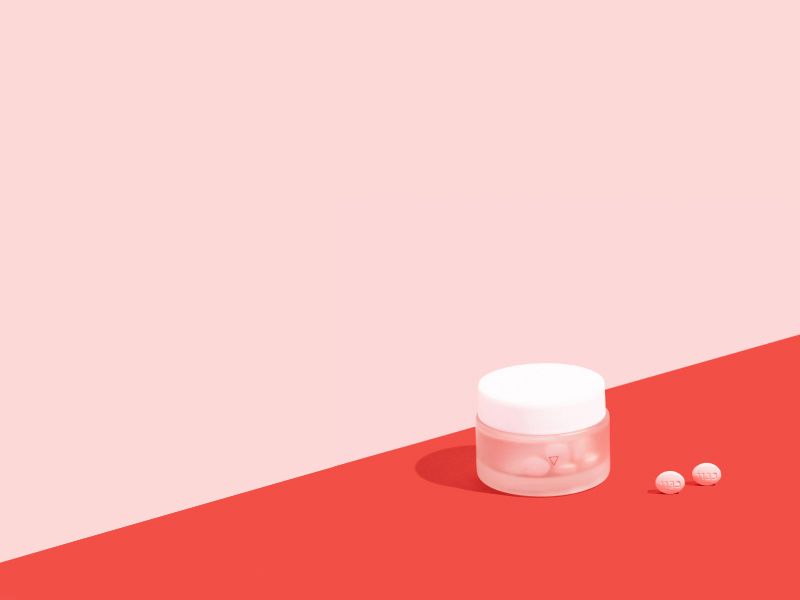 Wisp glass jar on pink and red surface with two pills outside the bottle