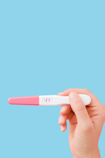 A woman's hand holding a pregnancy test in front of a light blue background