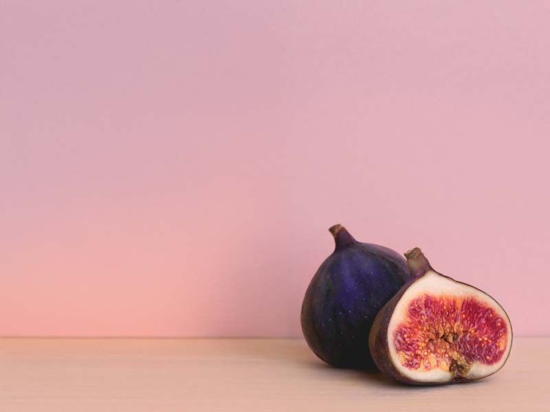 A cut open fig on a wood surface with mauve background