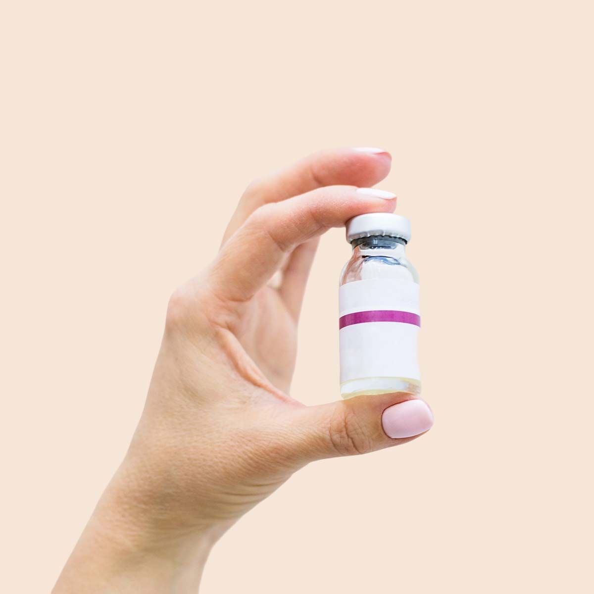 A person's hand holding an injection vial in front of a cream background