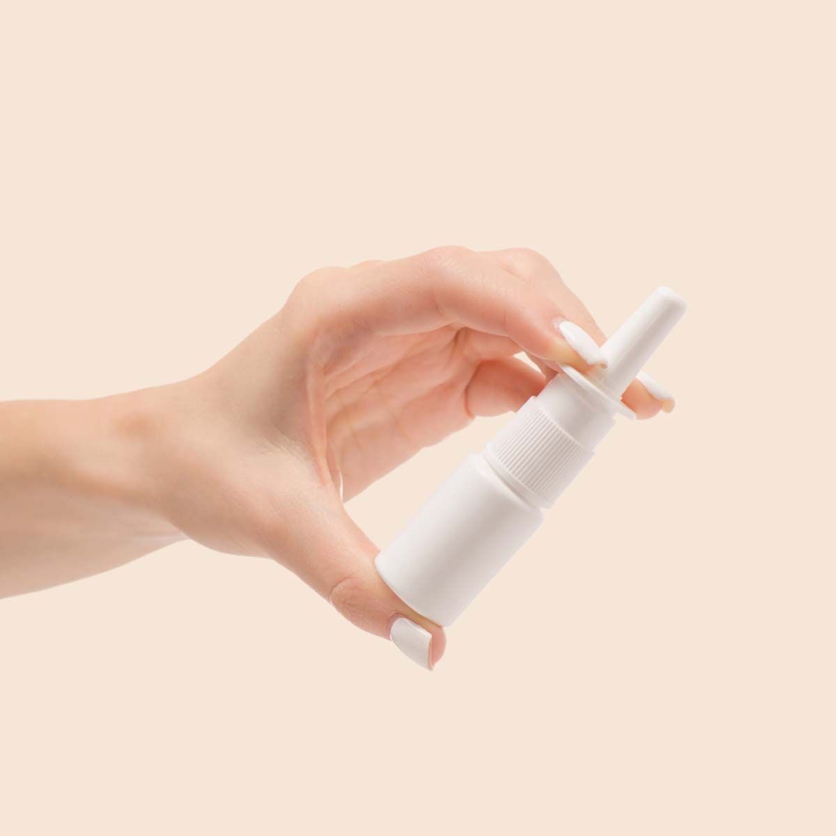 A person's hand holding a white nasal spray bottle with a cream background