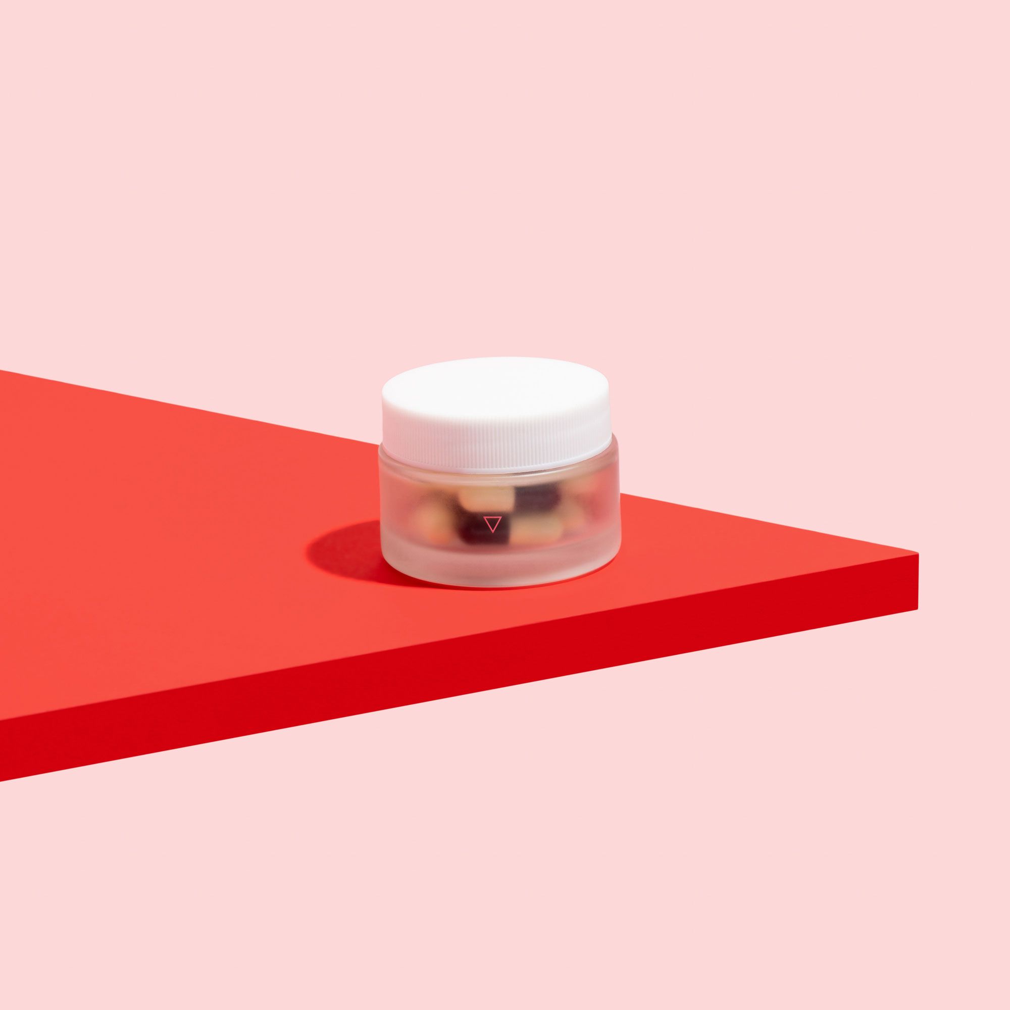 A glass pill jar of UTI antibiotics to treat urinary tract infections on a pink background and red surface