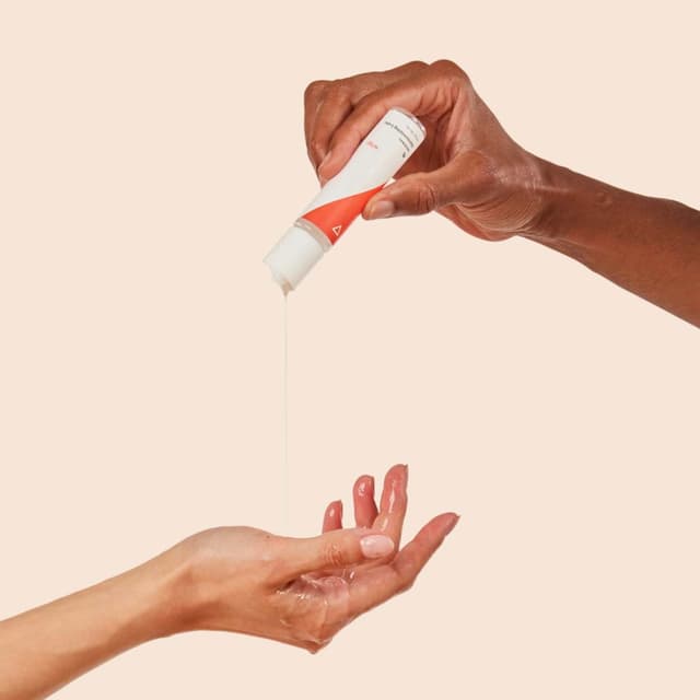A person squeezing lube into another person's hand with a cream background