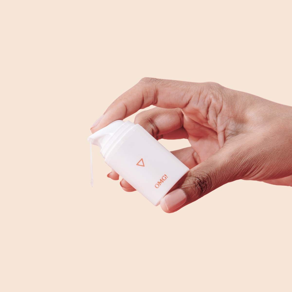 Woman's hand squeezes bottle of Wisp OMG! Cream while cream drips out on a cream background