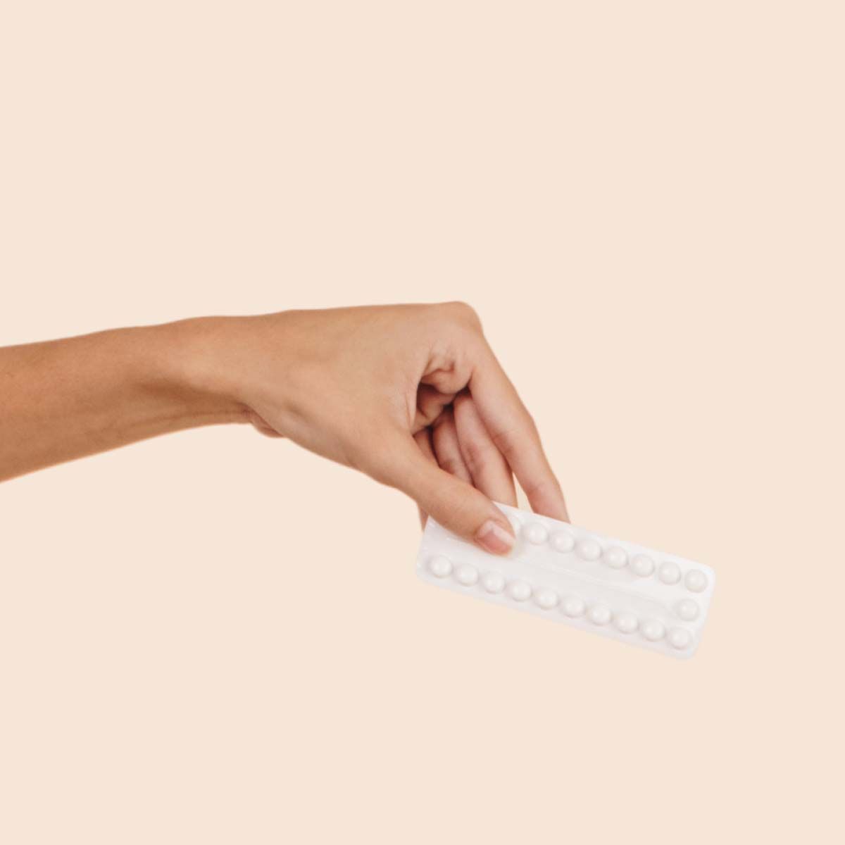 A person's hand holding Ortho Tri-Cycolin Lo birth control on a cream background