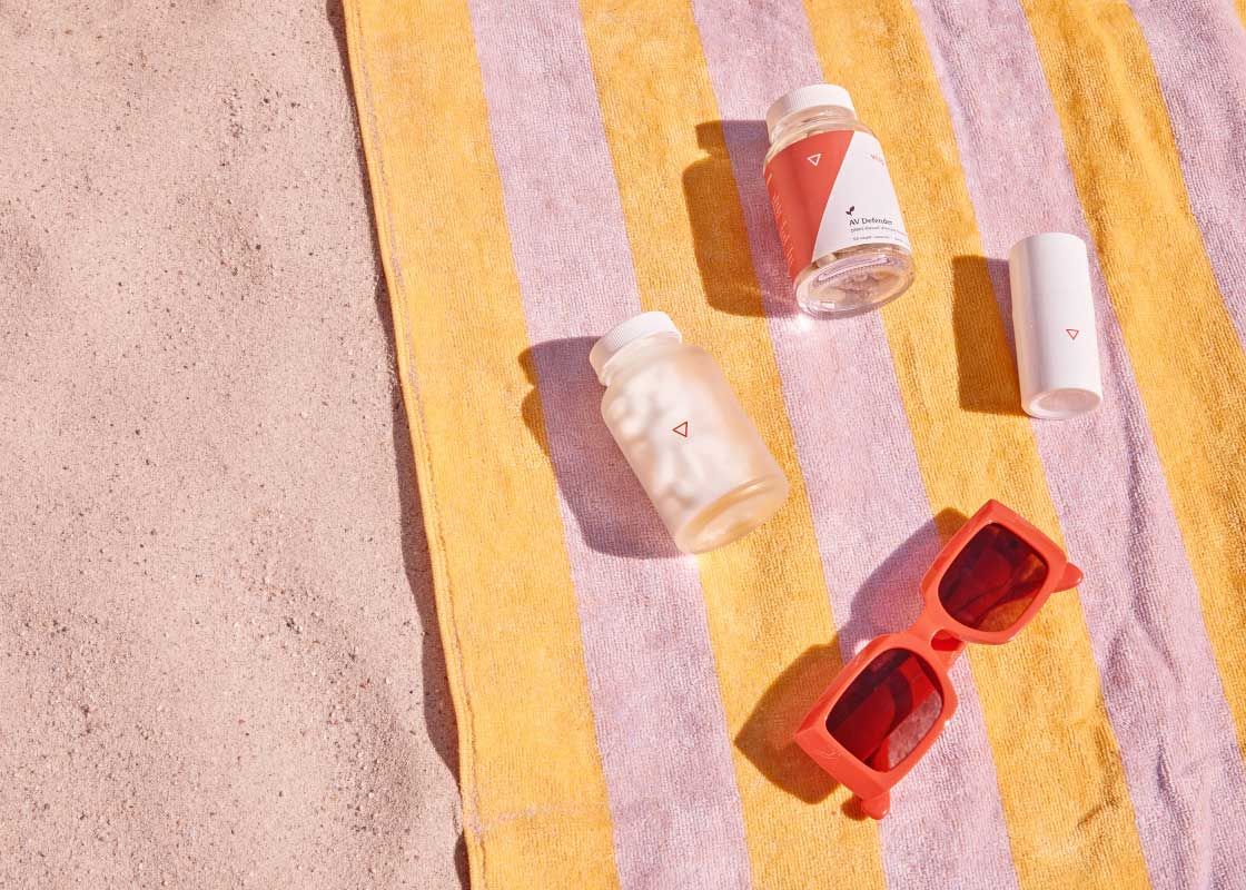 3 Wisp products and red sunglasses on a pink and yellow striped beach town laying on sand