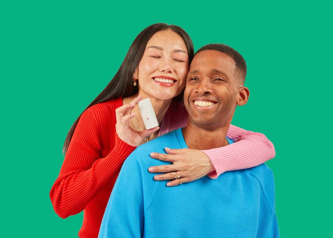 A woman wearing a pink and red sweater is holding a Wisp pump bottle next to her partner who is wearing a blue sweater