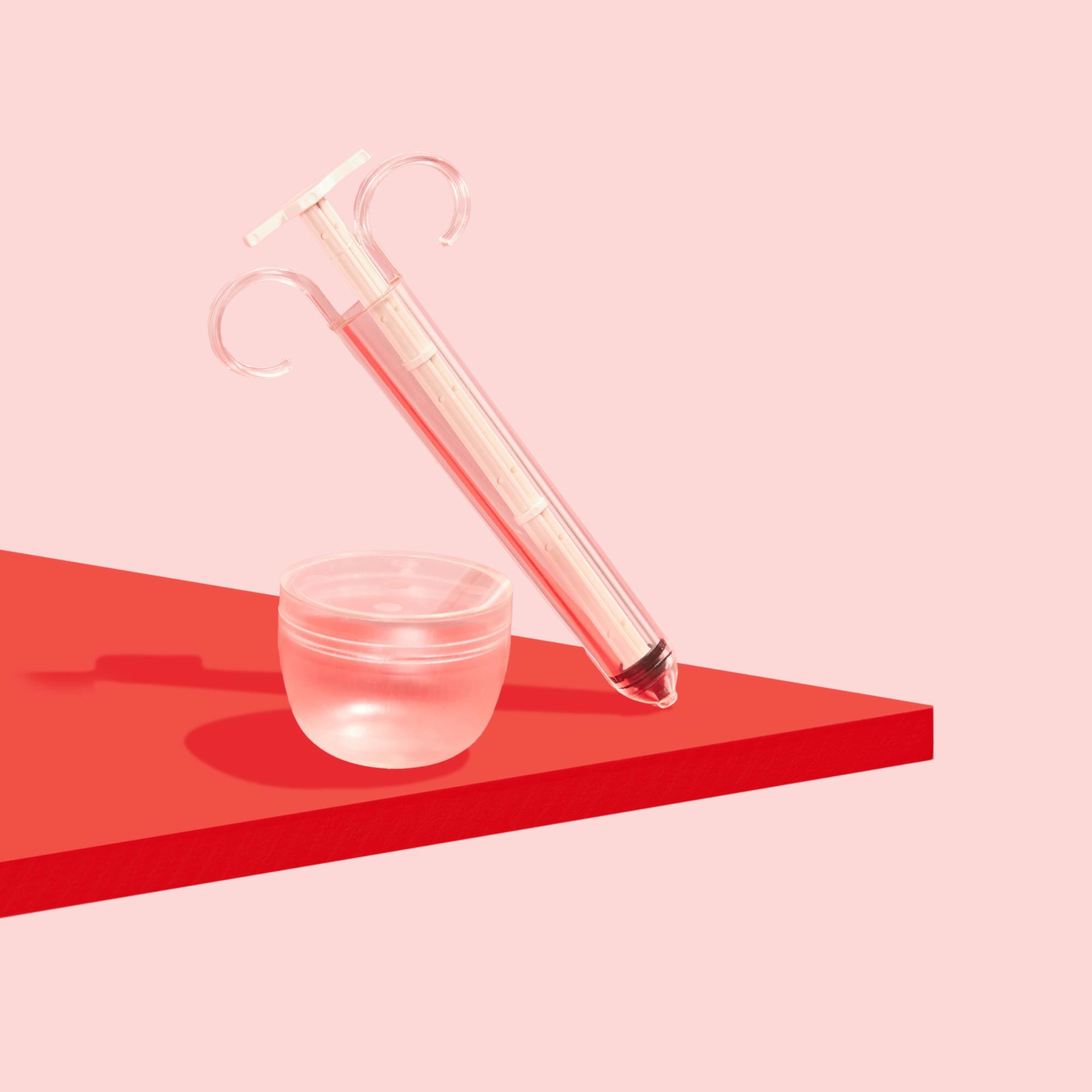 Pherdal collection cup and syringe on a red surface with a pink background