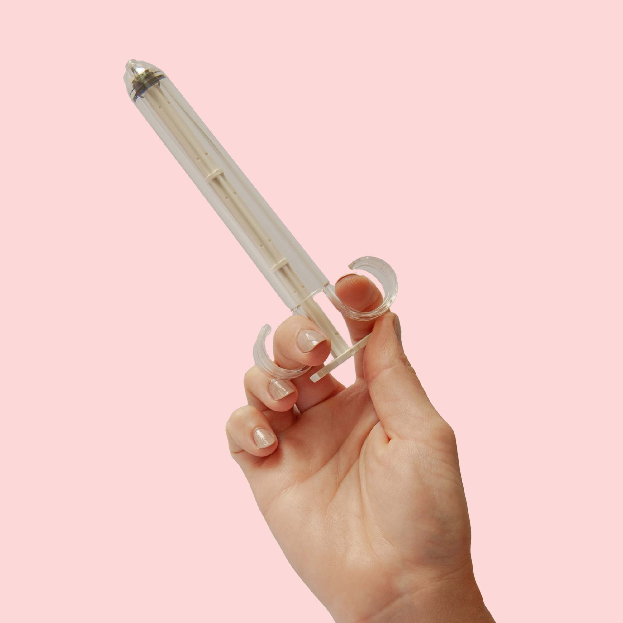 A woman's hand holding the Pherdal insemination syringe in front of a pink background