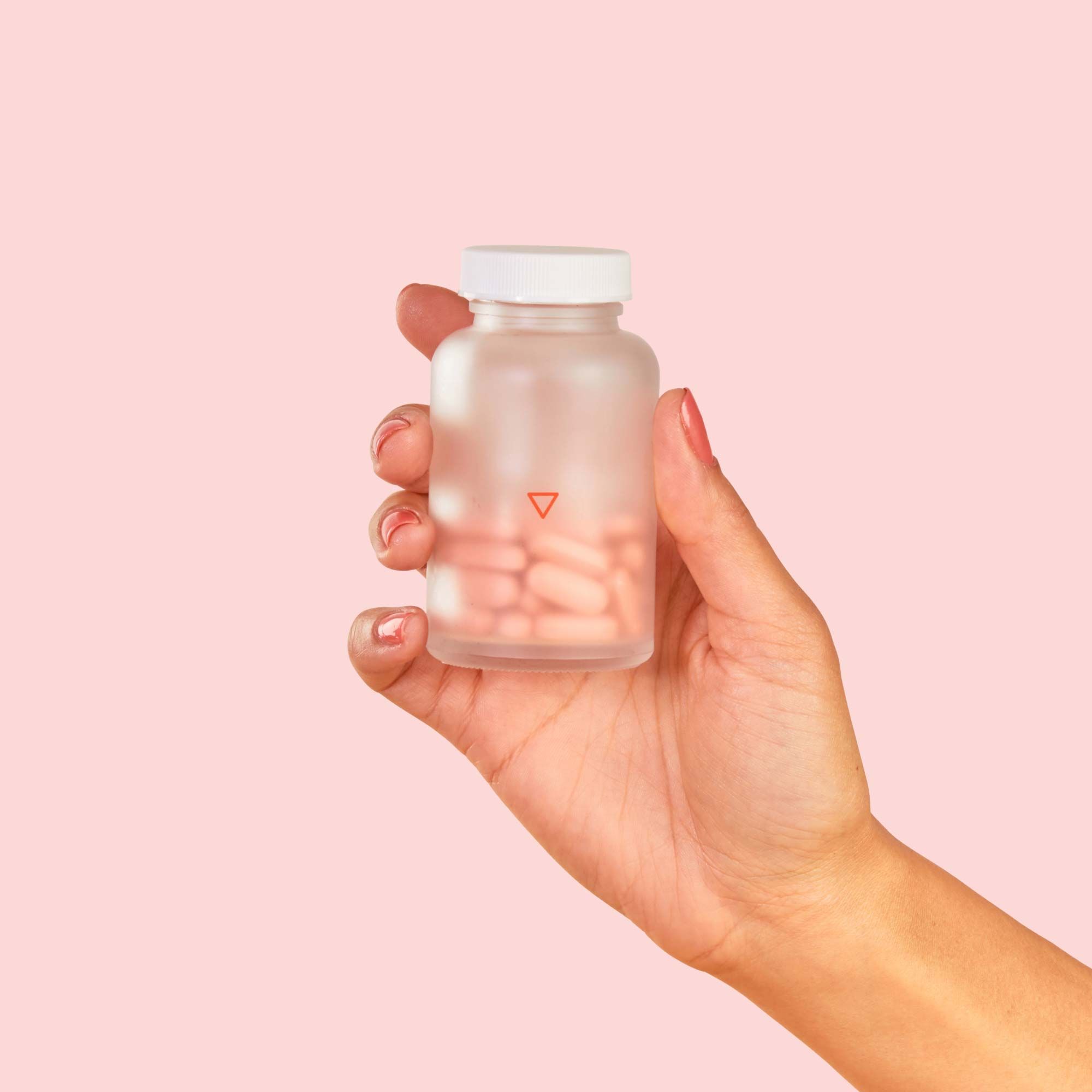 A woman's hand holding Wisp Prenatal Vitamins in front of a pink background