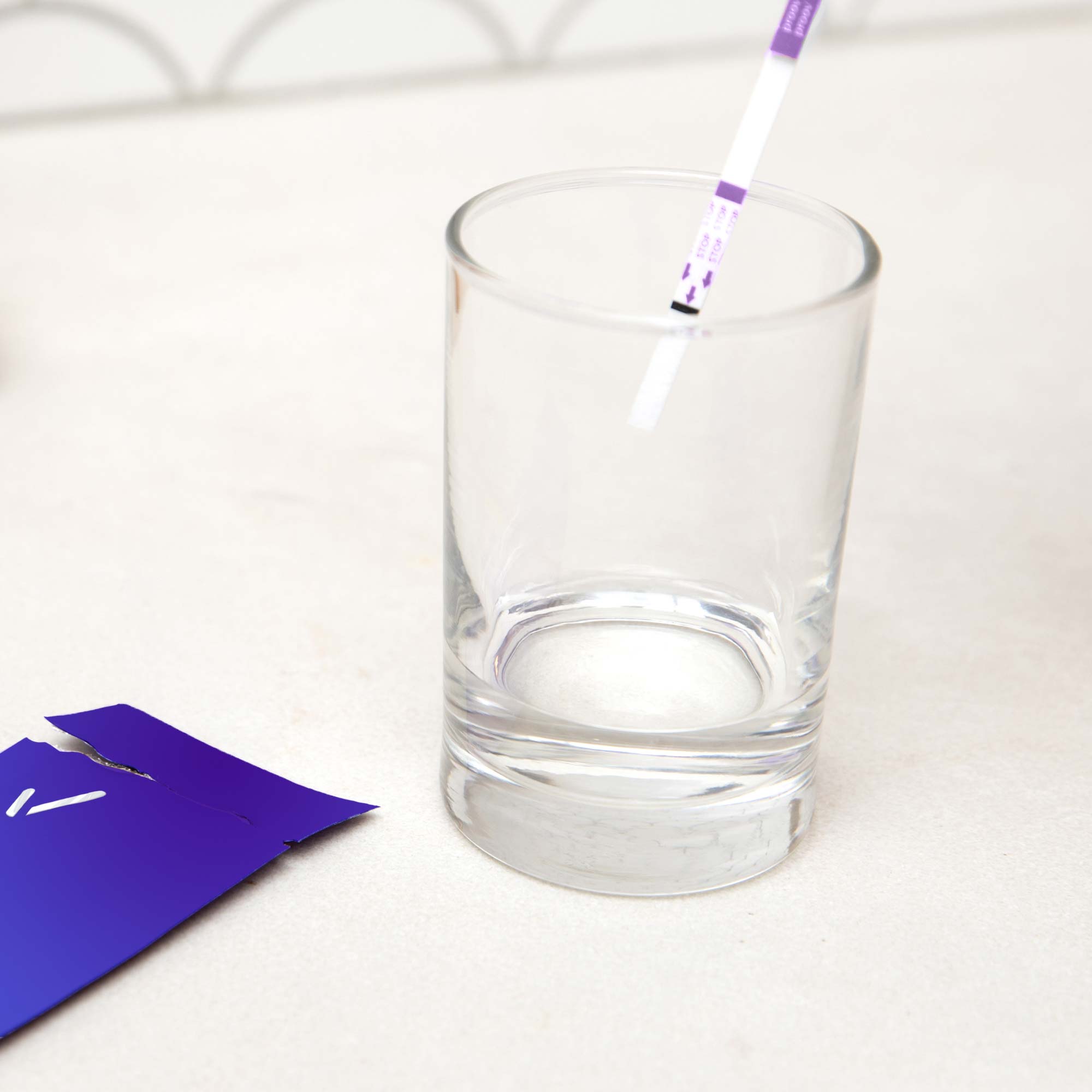 A test strip in a glass on a countertop with an opened Proov packet