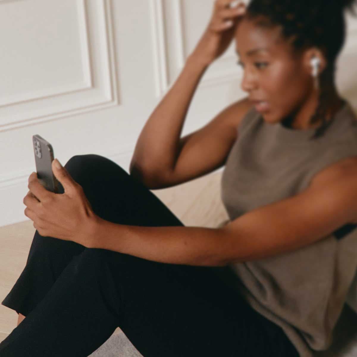 A woman wearing a gray short sleeve sweater and black pants is on a video call