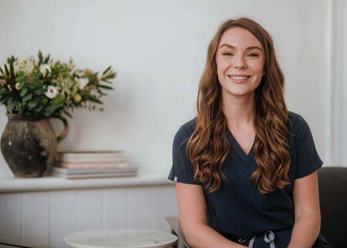Dr. Shannon Chatham, DO wearing dark blue scrubs sitting in an office with flowers and books in the background
