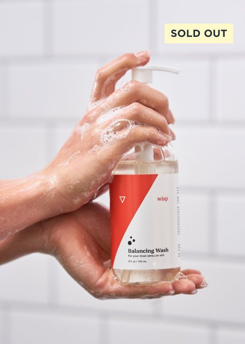 woman's hands lathered up with Wisp Balancing Wash holding bottle of wash in a white tile shower