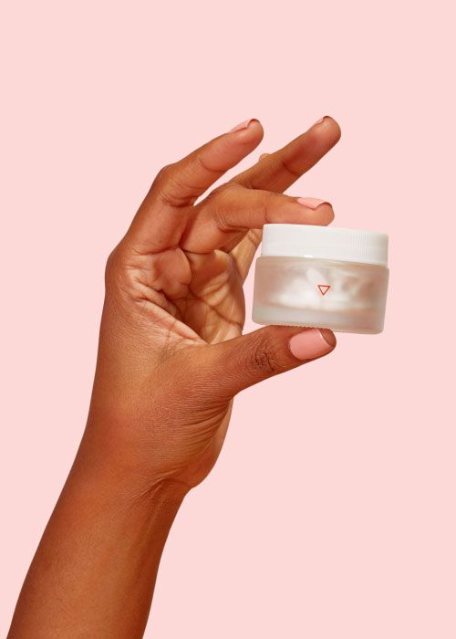 Woman's hand holds small glass jar of Wisp medicine on a pink background