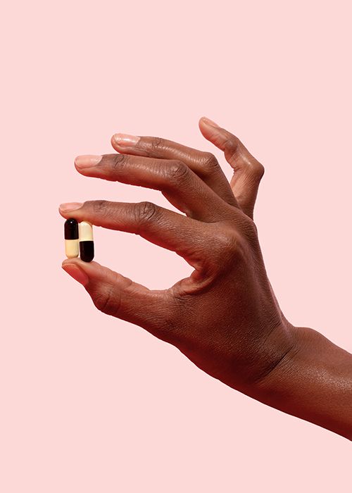 woman's hand holding antibiotics pills to treat UTI on a pink background