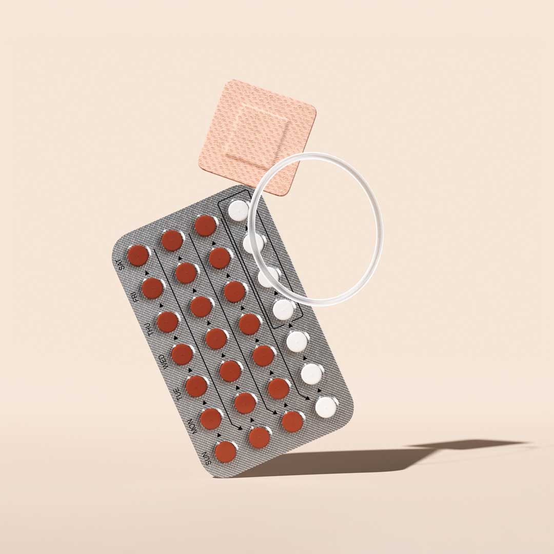 Birth control pill packet, patch, and ring balanced on a cream surface