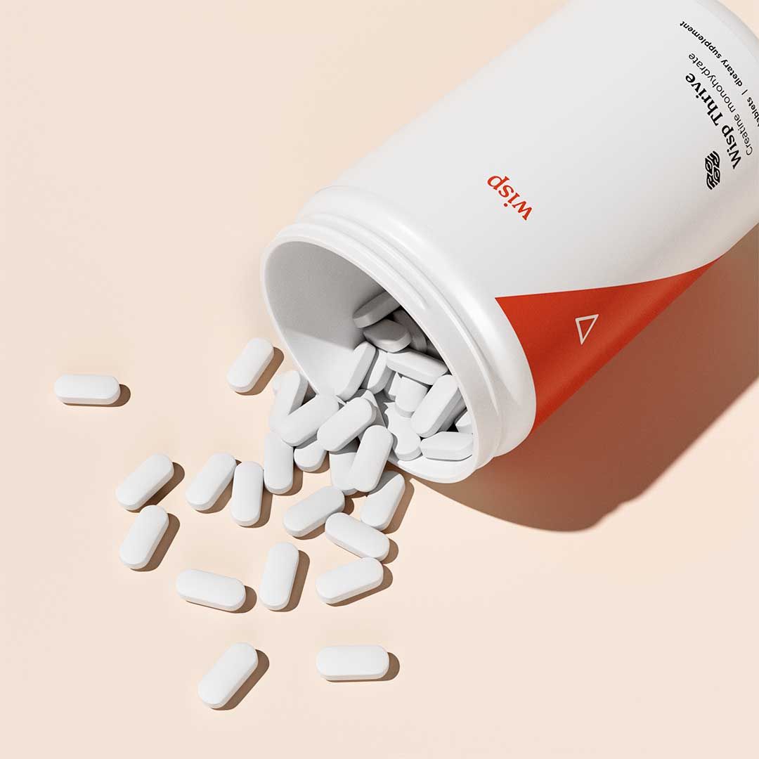 White pills spilling out of a bottle of Wisp Thrive Creatine on a cream surface