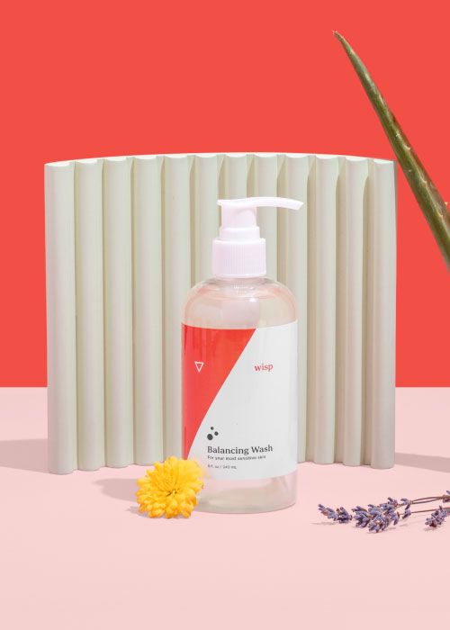 Wisp Balancing Wash with colorful abstract shapes, marigold, lavender, and aloe vera on a pink surface with a red background
