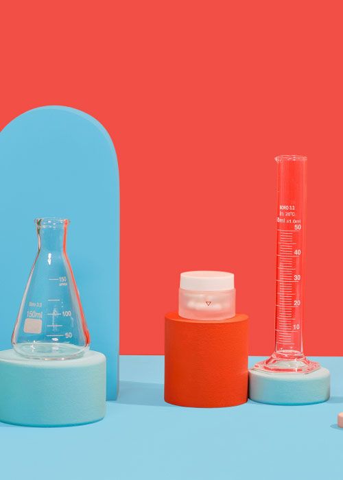 A small Wisp glass pill jar with test tubes balanced on colorful abstract shapes on a light blue surface with a red background