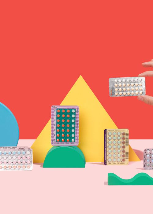 A woman's hand holding a birth control packet with several more balanced on colorful abstract shapes on a pink surface with a red background