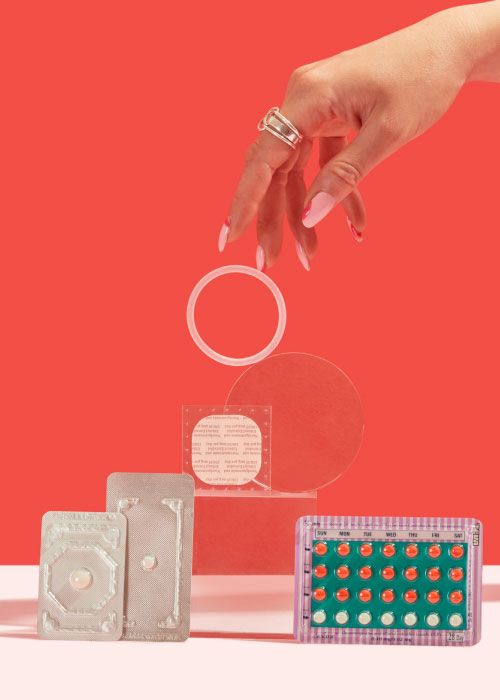 A woman's hand reaching for NuvaRing with the birth control patch, 2 emergency contraception packets and a birth control packet balanced on clear abstract shapes on a pink surface with a red background