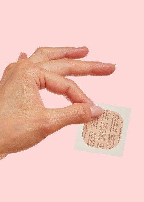 A woman's hand holding the birth control patch in front of a pink background