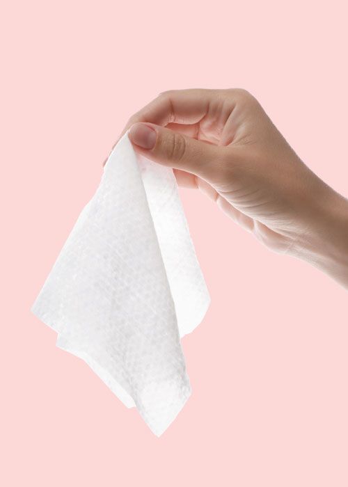 A woman's hand holding a pH wipe in front of a pink background