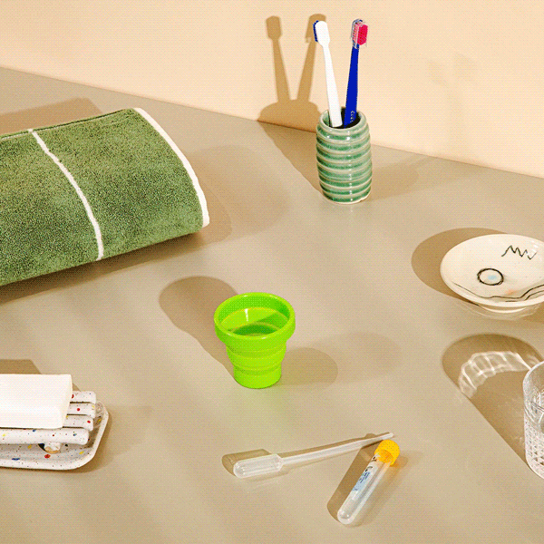 A person pouring water into a green collection cup to indicate a urine sample with test tubes and other miscellaneous kit items on a tan surface