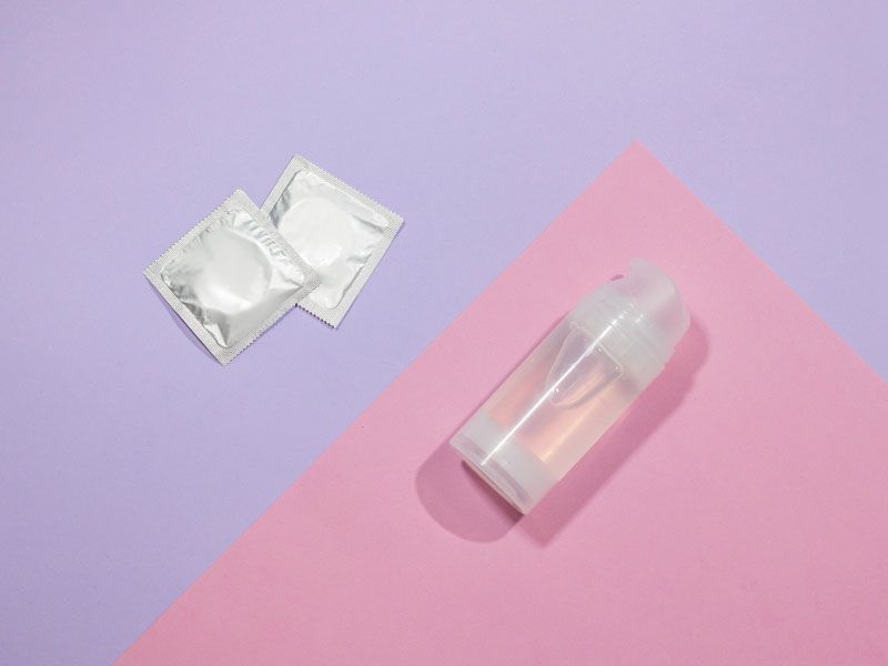 Bottle of clear liquid and 2 condoms on a pink and purple background