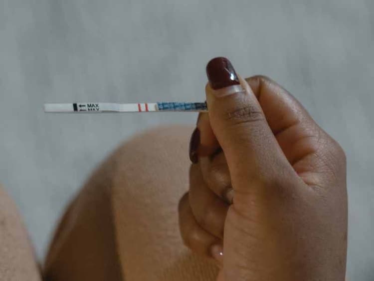 A woman's hand with painted nails holding a testing strip with an ambient background