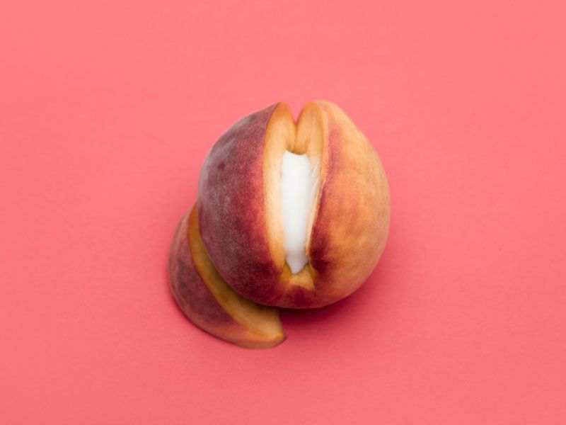 A cut open apricot with a cream substance in the middle on a red background